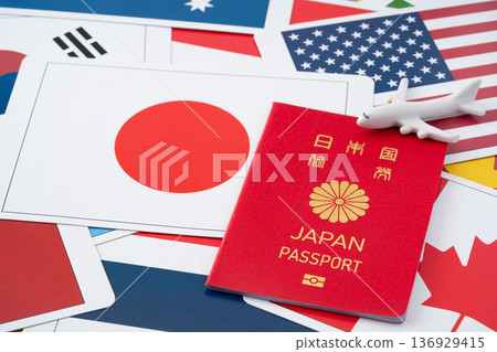 一本紅色的日本護照和一架微型飛機，背景是許多國旗卡。 136929415