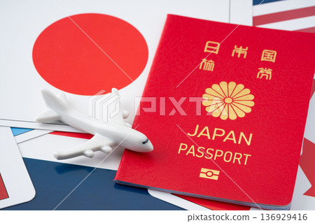 一本紅色的日本護照和一架微型飛機,背景是許多國旗卡。 一本紅色的日本護照和一架微型飛機,背景是許多國旗卡。 136929416