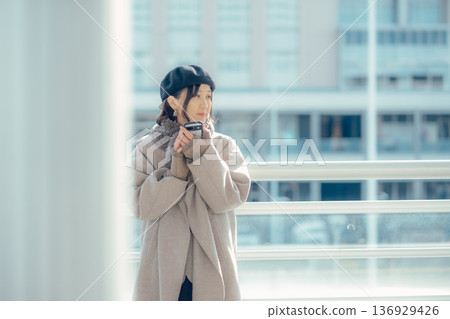 A woman checking her smartphone while waiting outdoors in winter A woman checking her smartphone while waiting outdoors in winter 136929426