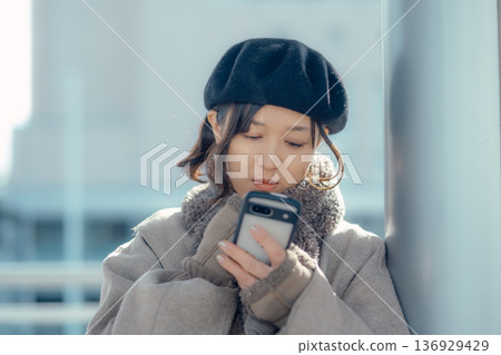 冬天,一位女士在戶外等候時正在查看智慧型手機。 冬天,一位女士在戶外等候時正在查看智慧型手機。 136929429