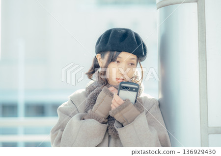 A woman checking her smartphone while waiting outdoors in winter A woman checking her smartphone while waiting outdoors in winter 136929430