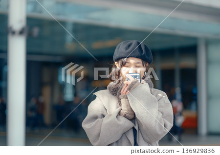 冬天，一位女士在戶外等候時正在查看智慧型手機。 136929836