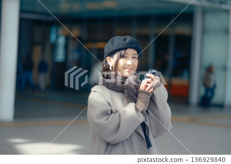 A woman checking her smartphone while waiting outdoors in winter A woman checking her smartphone while waiting outdoors in winter 136929840