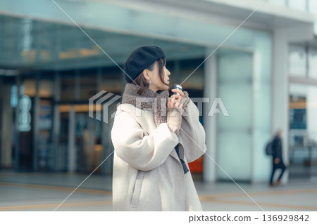 A woman checking her smartphone while waiting outdoors in winter A woman checking her smartphone while waiting outdoors in winter 136929842