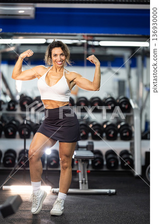 Woman flexing muscles showing strength and fitness in gym Woman flexing muscles showing strength and fitness in gym 136930000