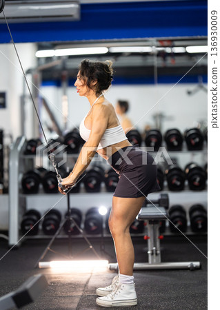 Woman training biceps with cable machine in gym Woman training biceps with cable machine in gym 136930009