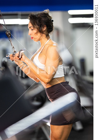 Woman training triceps at gym using cable machine Woman training triceps at gym using cable machine 136930011