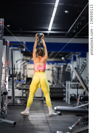 Woman exercising overhead dumbbell press in modern gym Woman exercising overhead dumbbell press in modern gym 136930113