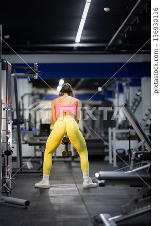 Woman exercising glutes with dumbbell at gym Woman exercising glutes with dumbbell at gym 136930116