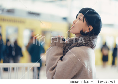 一位三十多歲的女子一邊喝咖啡一邊在車站內行走。 136930701