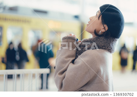 一位三十多歲的女子一邊喝咖啡一邊在車站內行走。 136930702