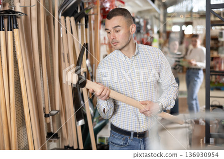 Amateur gardener man selects necessary items tools for her hobby in greenhouse flower-bed 136930954