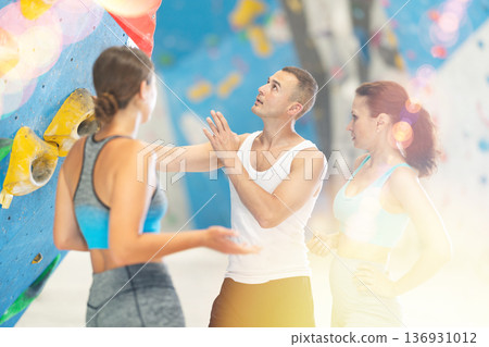 Young man and two women talking while standing at artificial climbing wall 136931012
