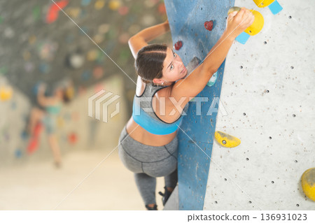 Young girl climbing on artificial rock wall in rock-climbing gym Young girl climbing on artificial rock wall in rock-climbing gym 136931023