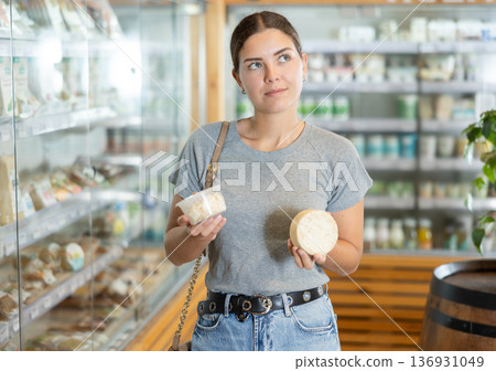 Positive young girl purchaser choosing cheese in large supermarket Positive young girl purchaser choosing cheese in large supermarket 136931049