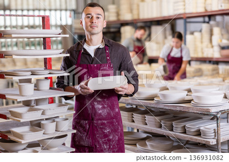 Artisan proudly showcasing collection of ceramic plates in workshop 136931082