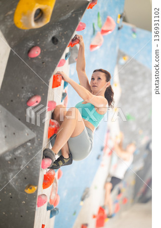 Middle-aged woman climbing on artificial rock wall in rock-climbing gym Middle-aged woman climbing on artificial rock wall in rock-climbing gym 136931102