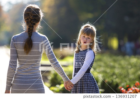 Moody cute child girl holding mother hand looking back on warm day outdoors. Family relationship and recreation. 136931207