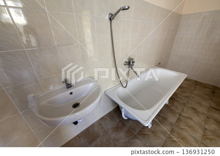 Interior of spacious light hospital or kindergarten bathroom with white bathtub, sink and tiled floor and walls. Interior of spacious light hospital or kindergarten bathroom with white bathtub, sink and tiled floor and walls. 136931250