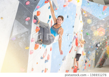 Young girl climbing on artificial rock wall in rock-climbing gym Young girl climbing on artificial rock wall in rock-climbing gym 136931278