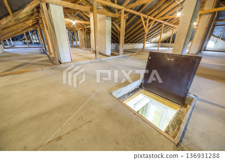 Attic of a building with wooden beams of a roof structure and a fire exit door in floor. 136931288