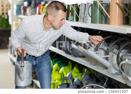 Amateur gardener man selects watering can for his hobby in greenhouse flower-bed Amateur gardener man selects watering can for his hobby in greenhouse flower-bed 136931307