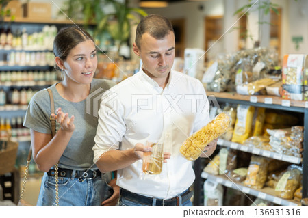 Positive couple discussing choice of pasta in organic foods store 136931316