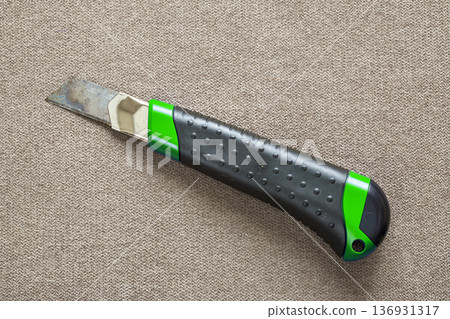 Close-up of isolated stationery retractable metallic knife with sharp blade on light cloth copy space background. Close-up of isolated stationery retractable metallic knife with sharp blade on light cloth copy space background. 136931317