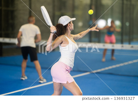 Woman with racket training on outdoor court playing padel game and hitting ball Woman with racket training on outdoor court playing padel game and hitting ball 136931327