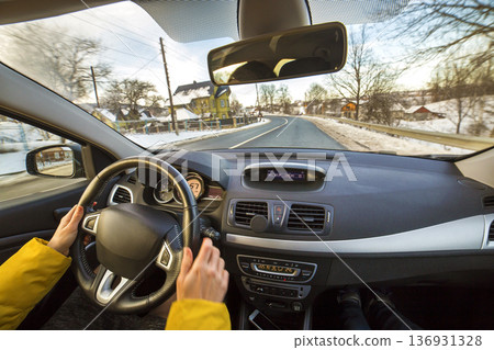 Modern car interior with driver female hands on steering wheel, winter snowy landscape outside. Safe driving concept. 136931328
