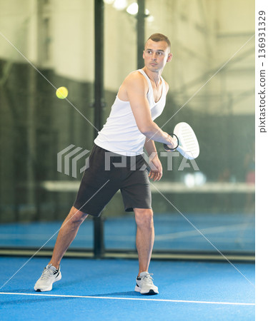 Active man with enthusiasm playing padel on tennis court 136931329