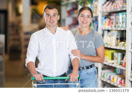 Married couple with trolley in trading floor browses eco product in bio shop search perfect goods 136931379