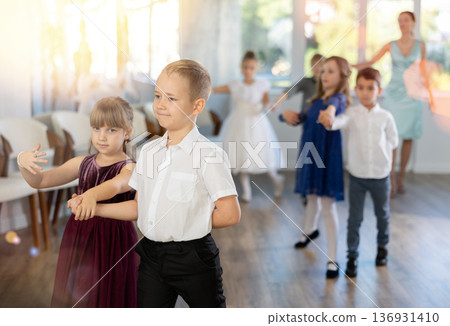 Little children in elegant dresses standing in pairs in dance pose in school hall Little children in elegant dresses standing in pairs in dance pose in school hall 136931410