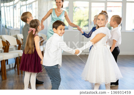 Smiling tweens dancing in round with female teacher during festive event 136931459