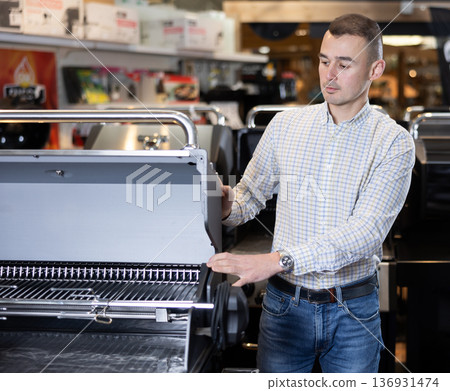 Satisfied customer in hypermarket chooses a barbecue grill for his backyard Satisfied customer in hypermarket chooses a barbecue grill for his backyard 136931474