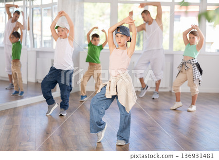 In sports studio, childrens team learns hip-hop dance accompanied by experienced man teacher In sports studio, childrens team learns hip-hop dance accompanied by experienced man teacher 136931481