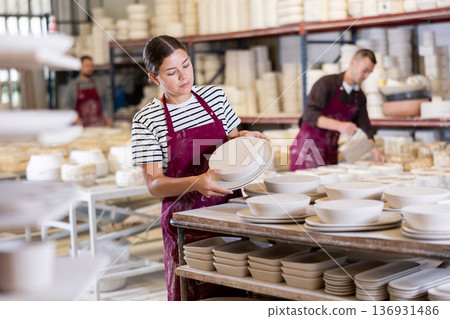 Female artisan stacking crafted ceramic plates on racks in workshop Female artisan stacking crafted ceramic plates on racks in workshop 136931486