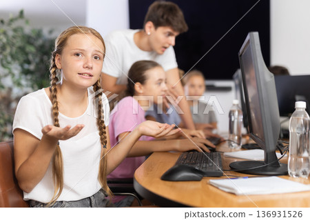 Confused preteen girl sitting at computer table in training room 136931526