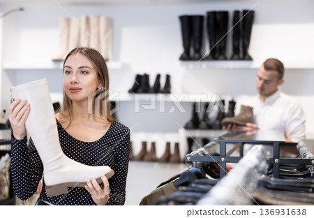 Girl buyer looks at footwear from new collection and picks up new pair of high boot Girl buyer looks at footwear from new collection and picks up new pair of high boot 136931638