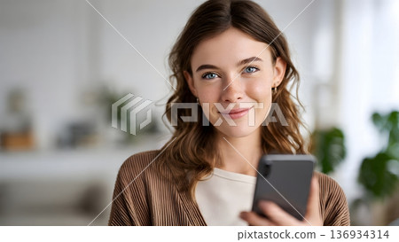 A cheerful young woman with bright blue eyes and natural freckles smiles genuinely while holding her smartphone. Her happy and content expression conveys a sense of positive connection. AI Generated 136934314