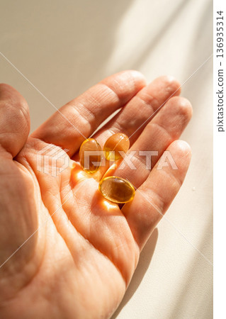 Close-up of woman's hand holding capsules with nutritional supplements, warm sunlight. A healthy lifestyle, daily vitamin intake preventative medicine 136935314