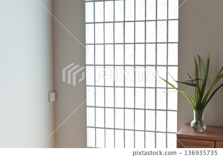 Glass block window natural light minimalist interior wooden cabinet green plant modern home clean wall bright room simple decor peaceful atmosphere 136935735