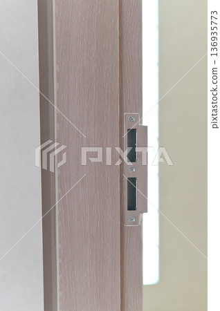 Wooden door frame metal strike plate closeup vertical light brown modern interior home security latch detail minimalist style soft lighting smooth texture residential safety construction Wooden door frame metal strike plate closeup vertical light brown modern interior home security latch detail minimalist style soft lighting smooth texture residential safety construction 136935773