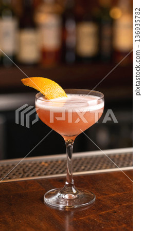 Pink cocktail with orange peel garnish on wooden bar counter. Refreshing alcoholic drink for happy hour. Pink cocktail with orange peel garnish on wooden bar counter. Refreshing alcoholic drink for happy hour. 136935782