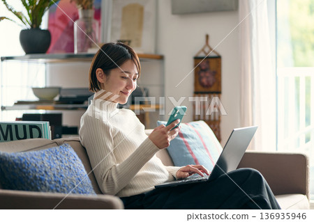 A woman holding a smartphone while operating a computer A woman holding a smartphone while operating a computer 136935946