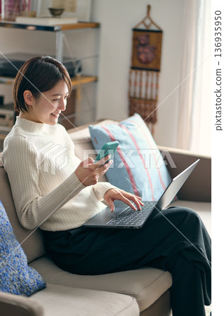 一名女子一邊操作電腦一邊拿著智慧型手機。 136935950