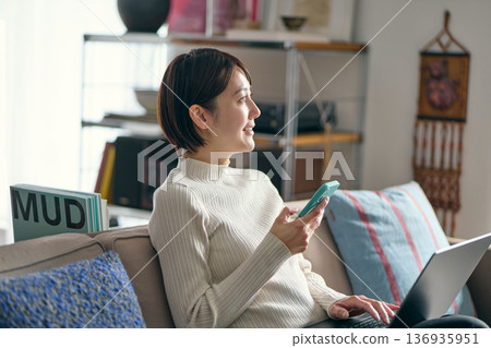 A woman holding a smartphone while operating a computer A woman holding a smartphone while operating a computer 136935951