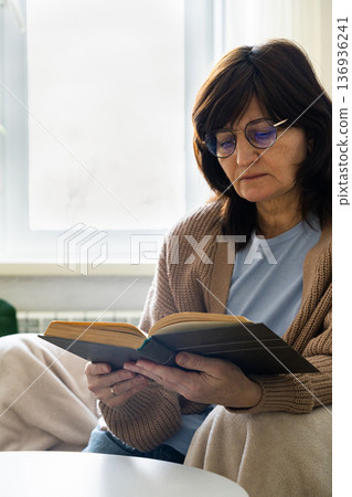 Woman wearing glasses reading book at home Woman wearing glasses reading book at home 136936241