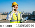 Smiling construction site supervisor holding a tablet and making a phone call on the rooftop Japanese male Construction management DX Urban development 136936549