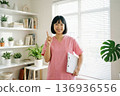 A Japanese female nurse/healthcare worker in a pink scrub smiling and pointing with her finger 136936556